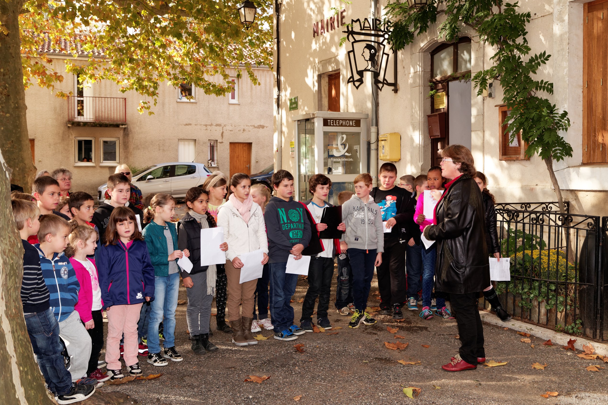 Les élèves de l'école entonnent la Marseillaise sous la direction de leur institutrice.
